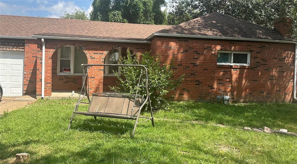 back of house with roof with shingles, an attached garage, a chimney, a lawn, and brick siding