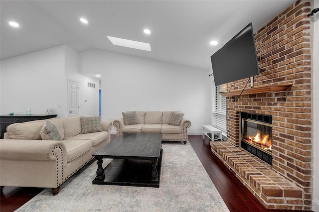 living room with visible vents, lofted ceiling with skylight, dark wood finished floors, recessed lighting, and a brick fireplace