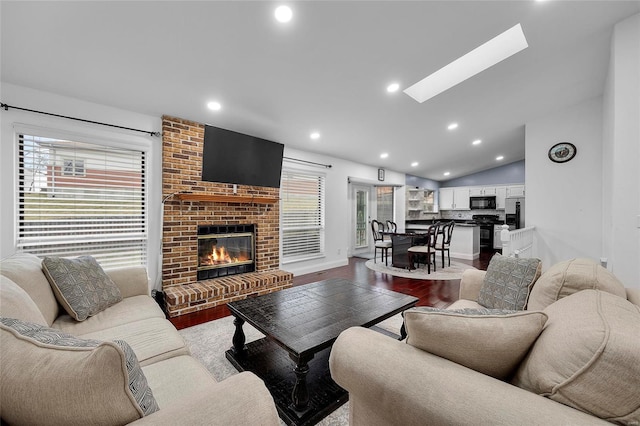 living room featuring a fireplace, vaulted ceiling with skylight, recessed lighting, and wood finished floors