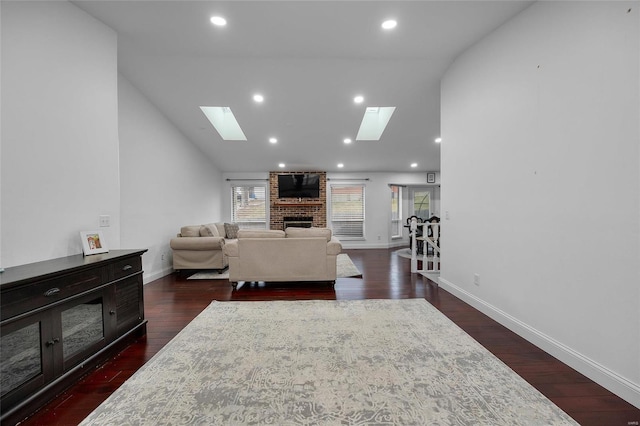 living room featuring high vaulted ceiling, dark wood-style floors, a skylight, baseboards, and a brick fireplace