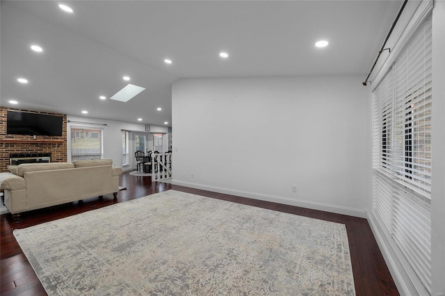 living room featuring recessed lighting, lofted ceiling with skylight, a brick fireplace, and dark wood finished floors