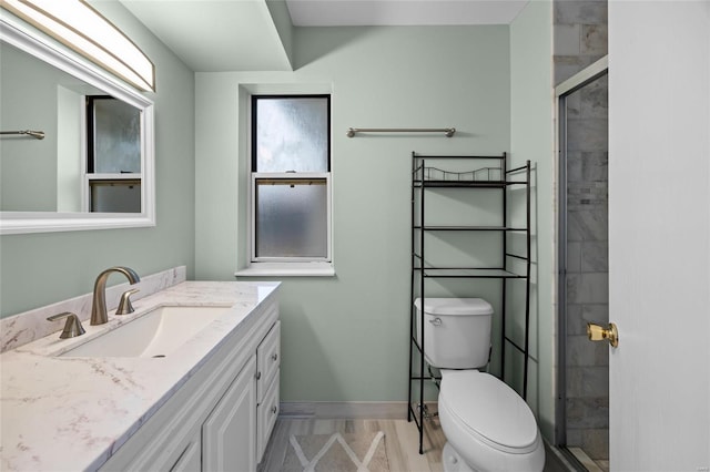 bathroom featuring toilet, wood finished floors, a tile shower, baseboards, and vanity