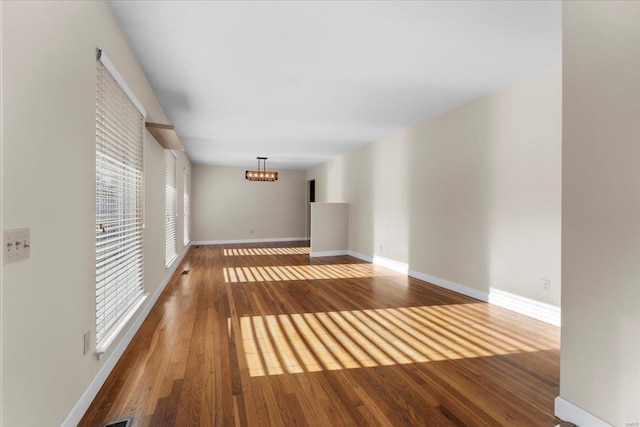 empty room with wood finished floors, baseboards, and a chandelier