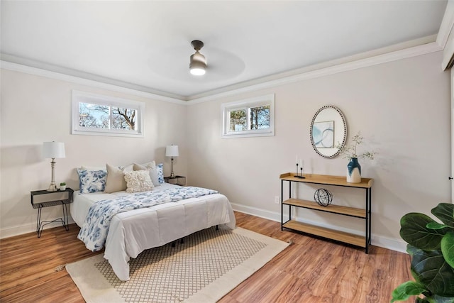 bedroom featuring multiple windows, baseboards, light wood finished floors, and ornamental molding