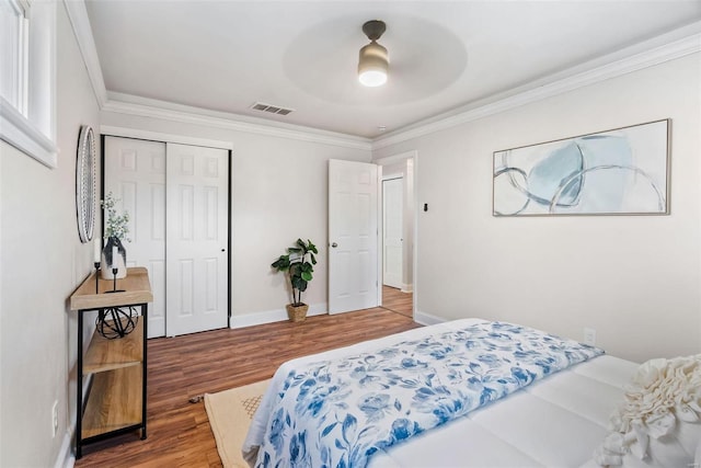 bedroom with visible vents, ornamental molding, wood finished floors, a closet, and baseboards