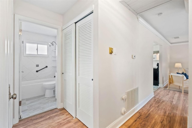 hall with baseboards, visible vents, light wood finished floors, and ornamental molding