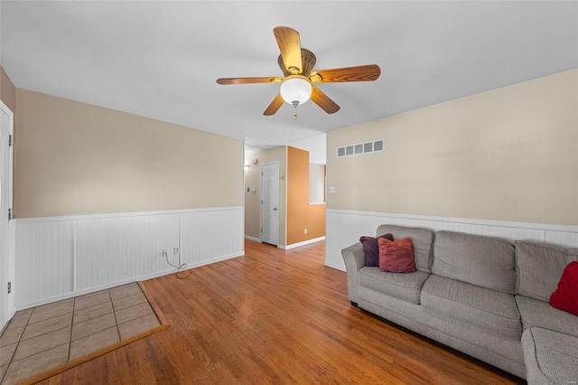 living room featuring visible vents, ceiling fan, a wainscoted wall, and wood finished floors