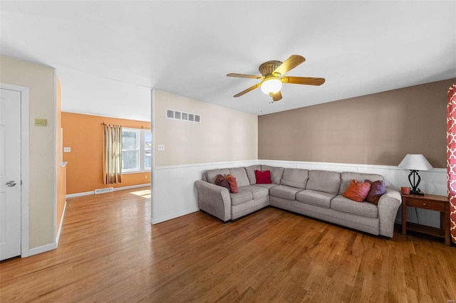 living room featuring light wood-type flooring, visible vents, baseboards, and a ceiling fan