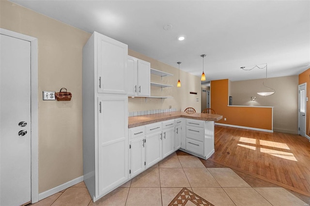 kitchen with open shelves, a peninsula, light tile patterned flooring, and white cabinetry