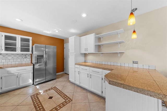 kitchen with stainless steel refrigerator with ice dispenser, backsplash, tile countertops, white cabinets, and light tile patterned floors