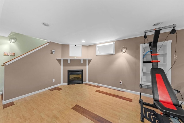 exercise room with a glass covered fireplace, crown molding, wood finished floors, and baseboards