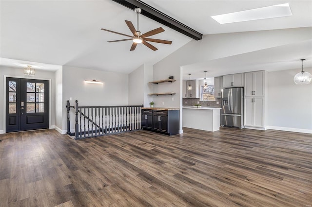 unfurnished living room featuring lofted ceiling with skylight, a ceiling fan, dark wood-type flooring, and baseboards