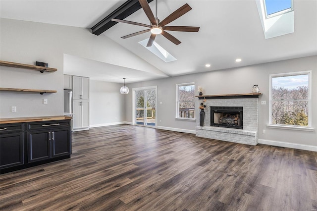 unfurnished living room featuring a brick fireplace, a skylight, a healthy amount of sunlight, and dark wood-style flooring