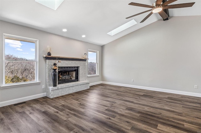 unfurnished living room with visible vents, baseboards, vaulted ceiling with skylight, a fireplace, and wood finished floors