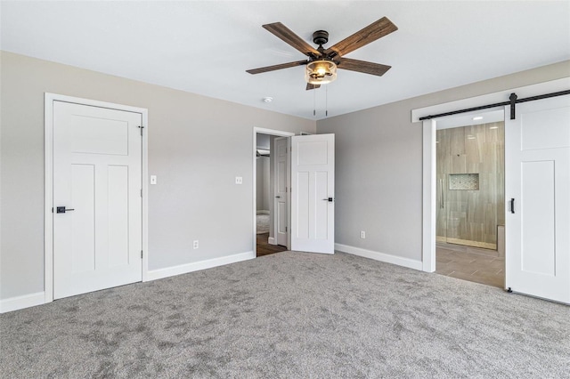 unfurnished bedroom featuring a barn door, baseboards, and carpet