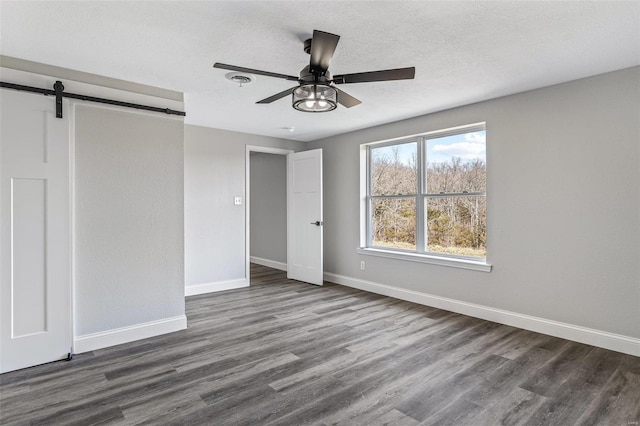 unfurnished bedroom with baseboards, dark wood-style flooring, ceiling fan, a textured ceiling, and a barn door