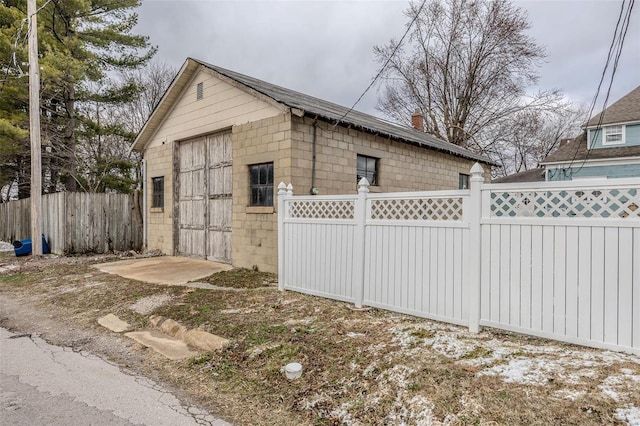 view of home's exterior featuring concrete block siding, a detached garage, fence, and an outbuilding