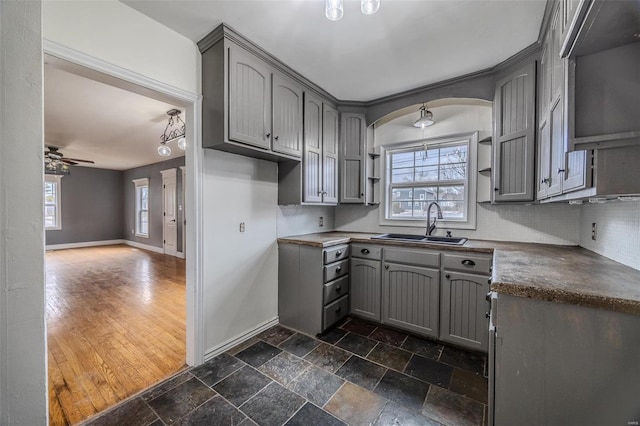 kitchen featuring stone tile flooring, gray cabinets, backsplash, and a sink