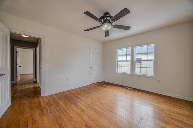 empty room featuring a ceiling fan, visible vents, wood finished floors, and baseboards