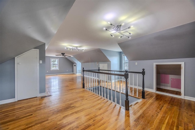 additional living space with vaulted ceiling, wood finished floors, baseboards, and visible vents