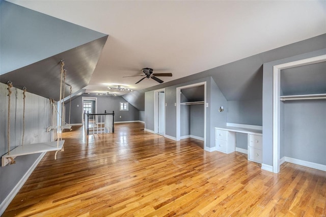 unfurnished living room with lofted ceiling, wood finished floors, built in desk, baseboards, and ceiling fan