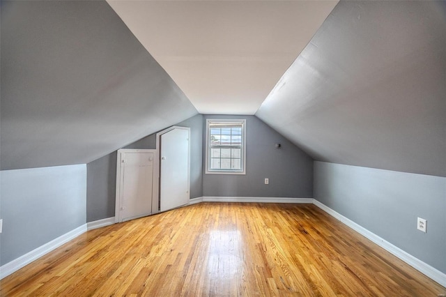 additional living space with baseboards, light wood-style floors, and vaulted ceiling