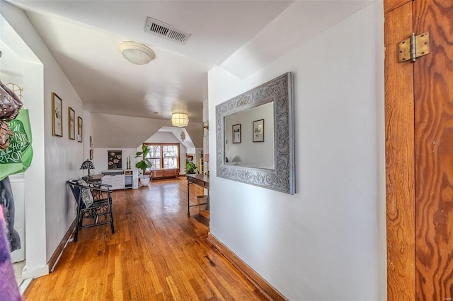 hallway with vaulted ceiling, baseboards, visible vents, and wood-type flooring