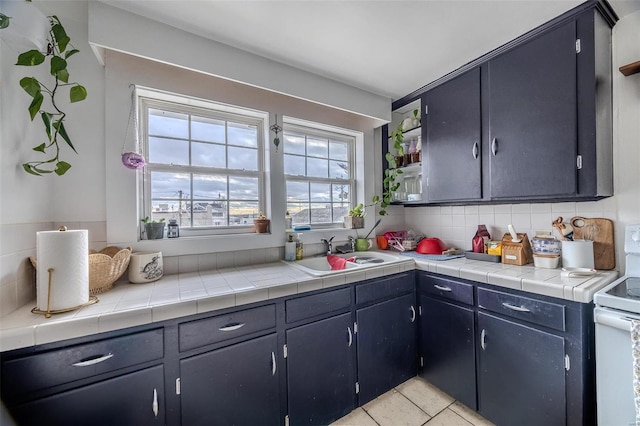 kitchen featuring electric stove, a sink, light countertops, light tile patterned floors, and decorative backsplash