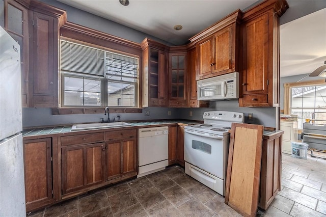 kitchen featuring brown cabinets, a sink, stone finish flooring, white appliances, and tile counters