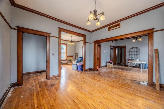 spare room featuring ornamental molding, light wood-style floors, an inviting chandelier, a fireplace, and baseboards