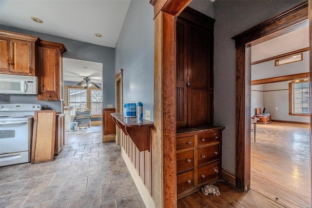 interior space with brown cabinets, a ceiling fan, stone finish flooring, white appliances, and baseboards