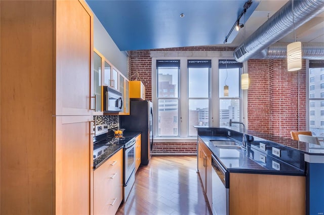 kitchen featuring a center island with sink, light wood finished floors, brick wall, a sink, and stainless steel appliances