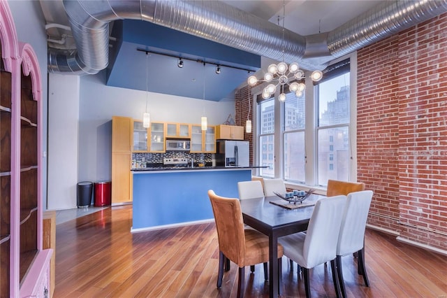 dining area featuring an inviting chandelier, wood finished floors, brick wall, and a healthy amount of sunlight