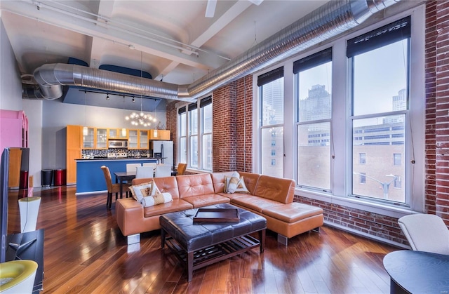 living area featuring brick wall, an inviting chandelier, dark wood-type flooring, rail lighting, and a towering ceiling