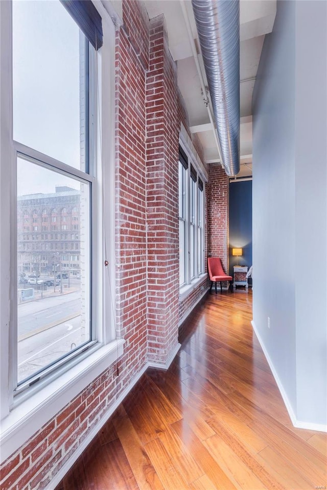 hall with wood finished floors, baseboards, and brick wall