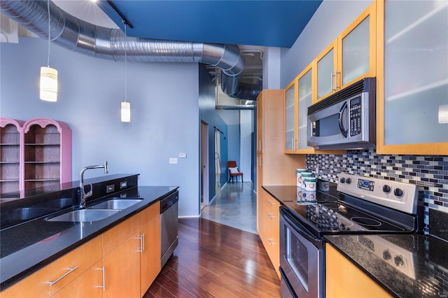 kitchen featuring dark wood finished floors, dark stone counters, a sink, appliances with stainless steel finishes, and backsplash