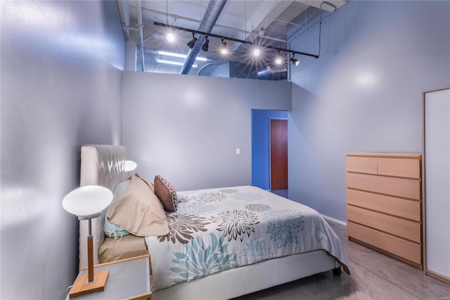 bedroom with track lighting, concrete flooring, and a towering ceiling