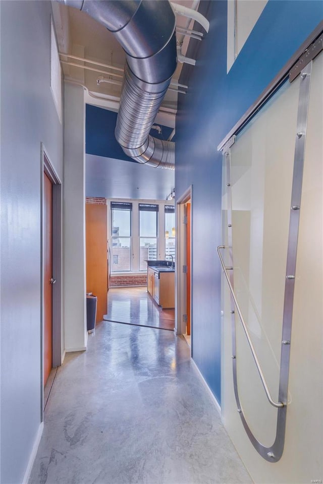 hall featuring a sink, baseboards, a high ceiling, and concrete flooring