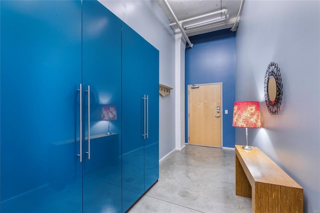 corridor with baseboards, concrete floors, and a towering ceiling