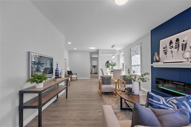 living area with a glass covered fireplace, baseboards, wood finished floors, and recessed lighting