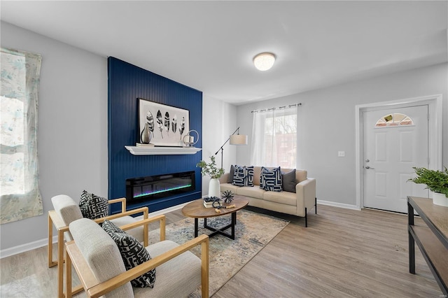 living room featuring a glass covered fireplace, baseboards, and wood finished floors