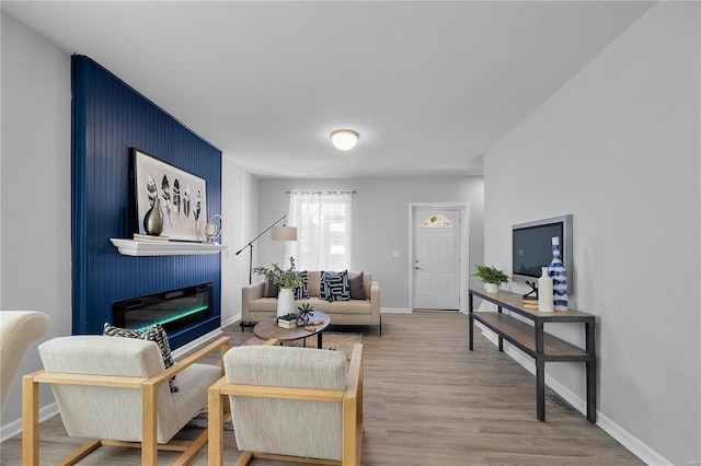 living room featuring a glass covered fireplace, wood finished floors, and baseboards