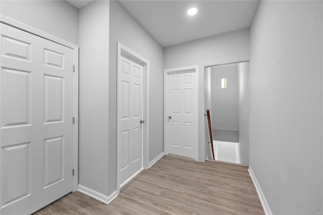 hall featuring an upstairs landing, light wood-type flooring, and baseboards