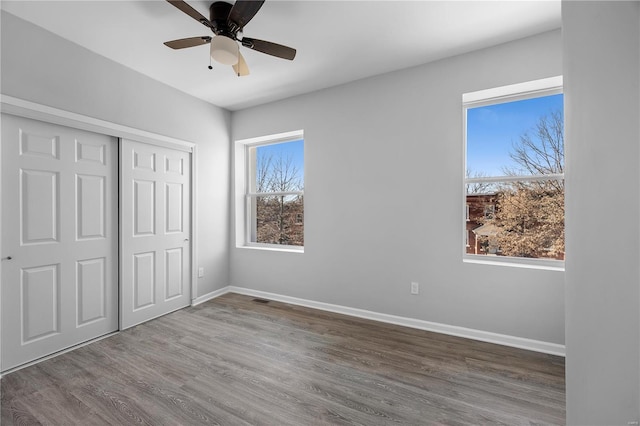 unfurnished bedroom featuring wood finished floors, visible vents, baseboards, ceiling fan, and a closet