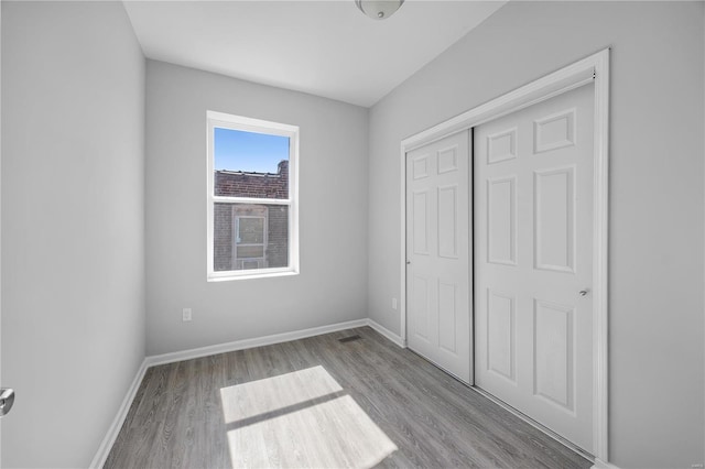 unfurnished bedroom with a closet, baseboards, visible vents, and wood finished floors