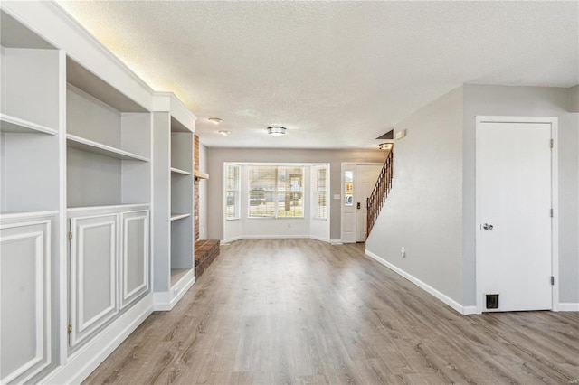 unfurnished living room with stairs, wood finished floors, baseboards, and a textured ceiling