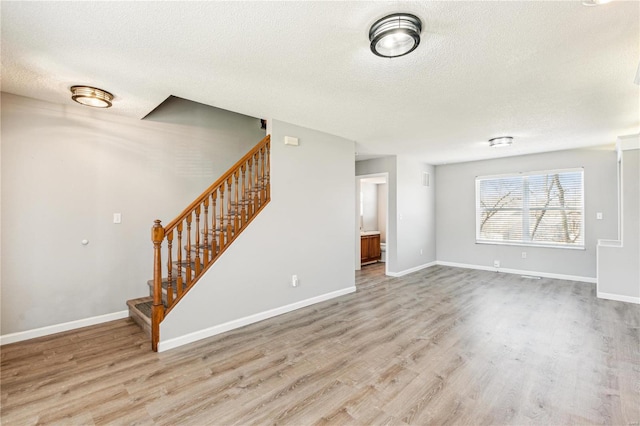 unfurnished living room with stairway, baseboards, and wood finished floors