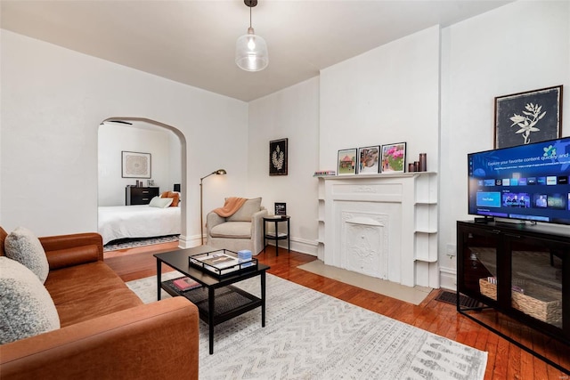 living room with a fireplace with flush hearth, wood finished floors, and arched walkways