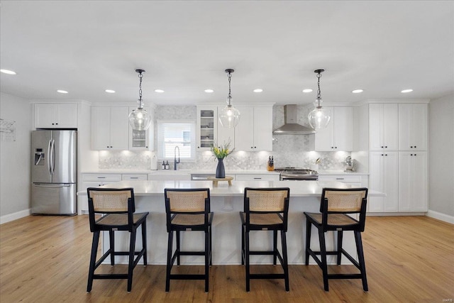 kitchen featuring a kitchen island, wall chimney range hood, light countertops, stainless steel refrigerator with ice dispenser, and stove