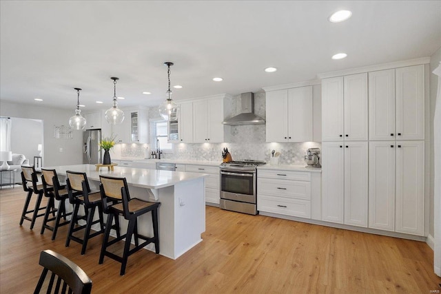 kitchen with a kitchen island, a breakfast bar, appliances with stainless steel finishes, white cabinetry, and wall chimney exhaust hood